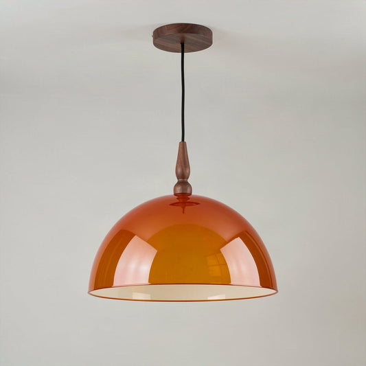 Amber acrylic dome pendant light with walnut finial hanging against a plain wall