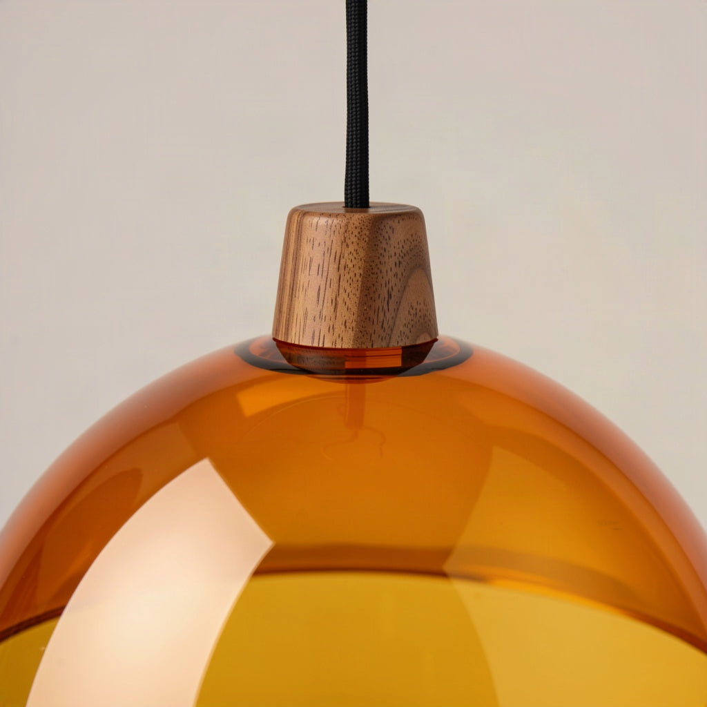 Close-up of the turned walnut finial where the black cord meets the amber acrylic dome