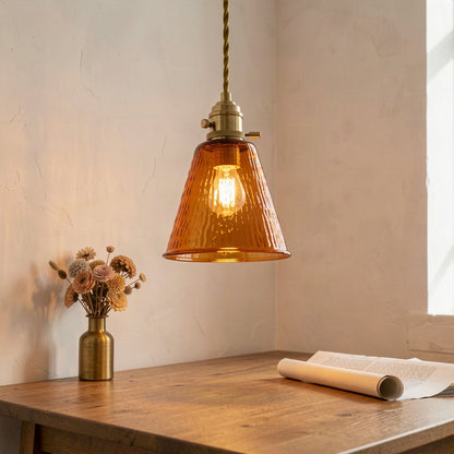 Amber glass pendant lit above a wooden desk in a corner of a room