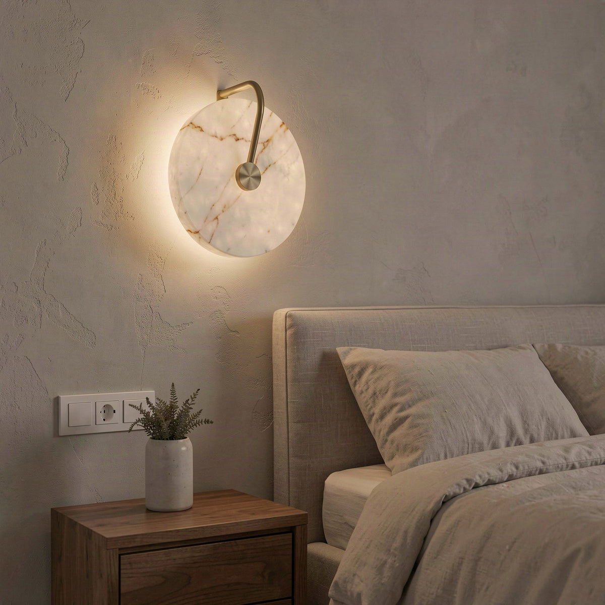 The marble disc wall light glowing warm white above a bedside table beside a linen bed