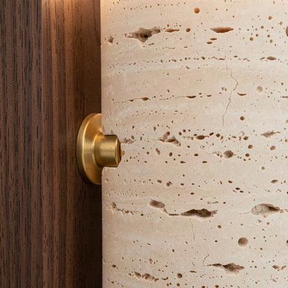 Close detail of the pitted travertine cylinder meeting the brass pivot and walnut backplate