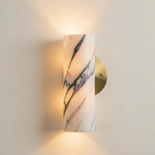Veined marble cylinder wall light on a brass wall plate, lit and washing light up and down the wall