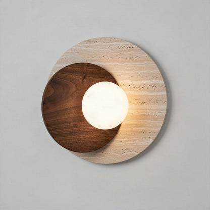Travertine and walnut disc wall light with an opal glass globe, lit against a pale wall