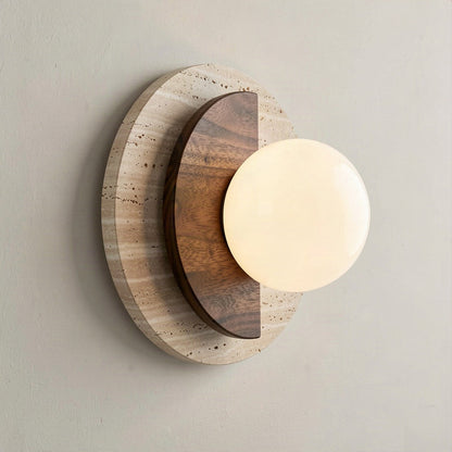 Angled view showing the wood disc lapping over the travertine disc and the globe projecting from the wall