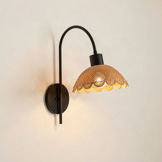 Woven rattan petal wall light on a curved black metal arm against a plain wall