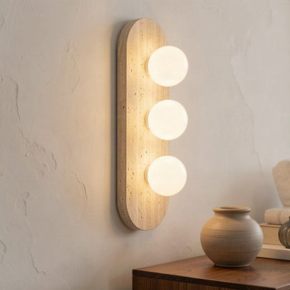 Three-light travertine wall light lit beside a console table in a plastered room