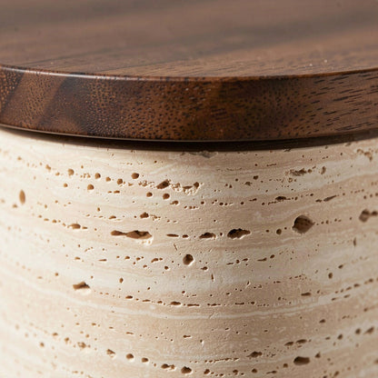 Close-up of the open-pored travertine surface meeting the turned walnut cap