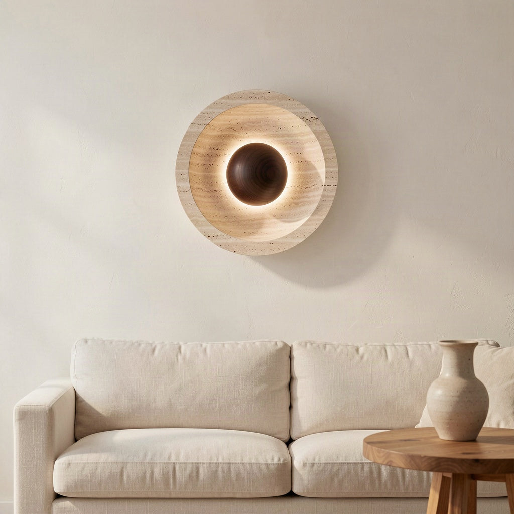 Travertine disc wall light lit above a sofa in a plain plastered living room