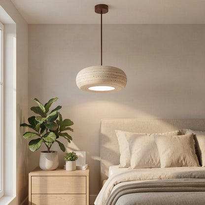 The travertine donut pendant hanging beside a bed in a warmly lit bedroom