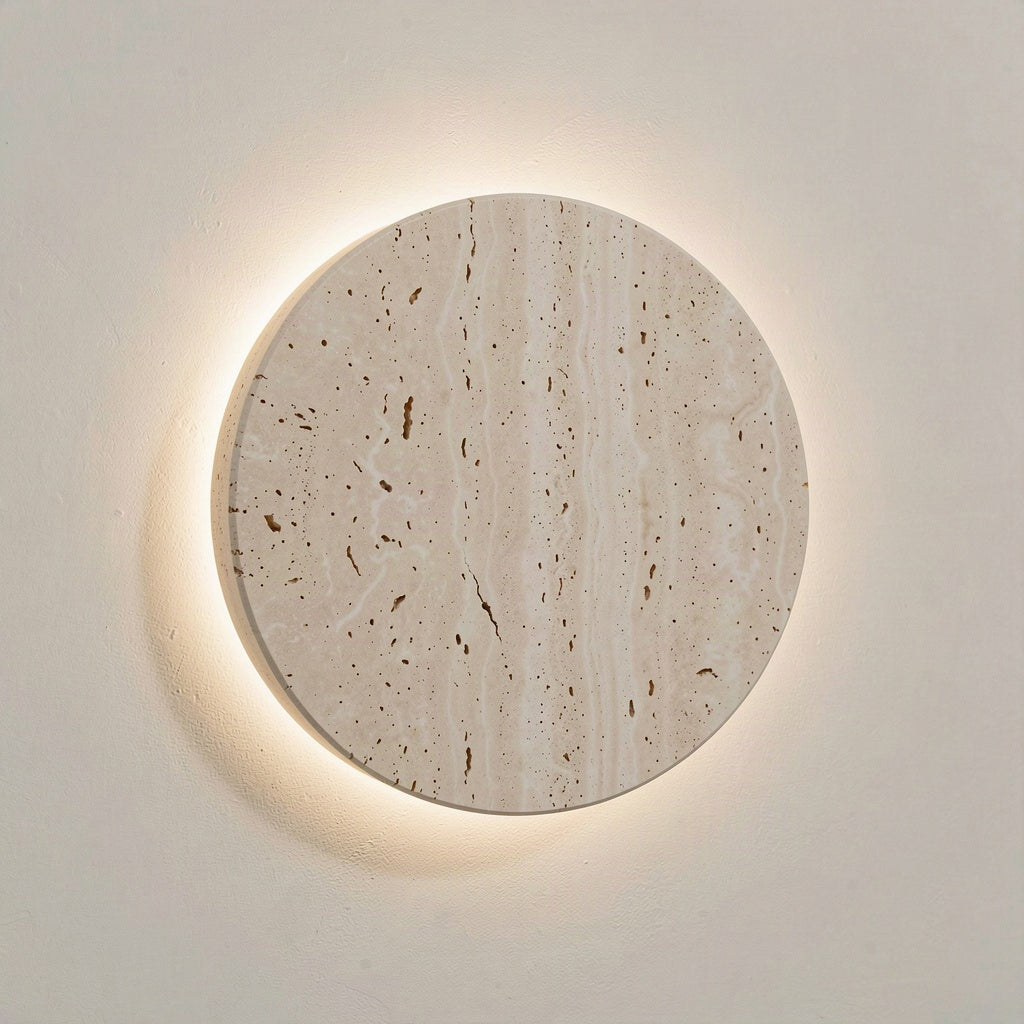 Round 25cm travertine disc wall light with a warm halo of light around its rim