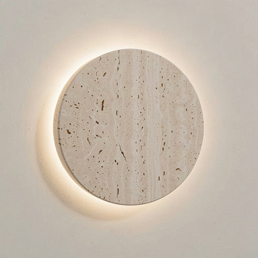 Round 25cm travertine disc wall light with a warm halo of light around its rim